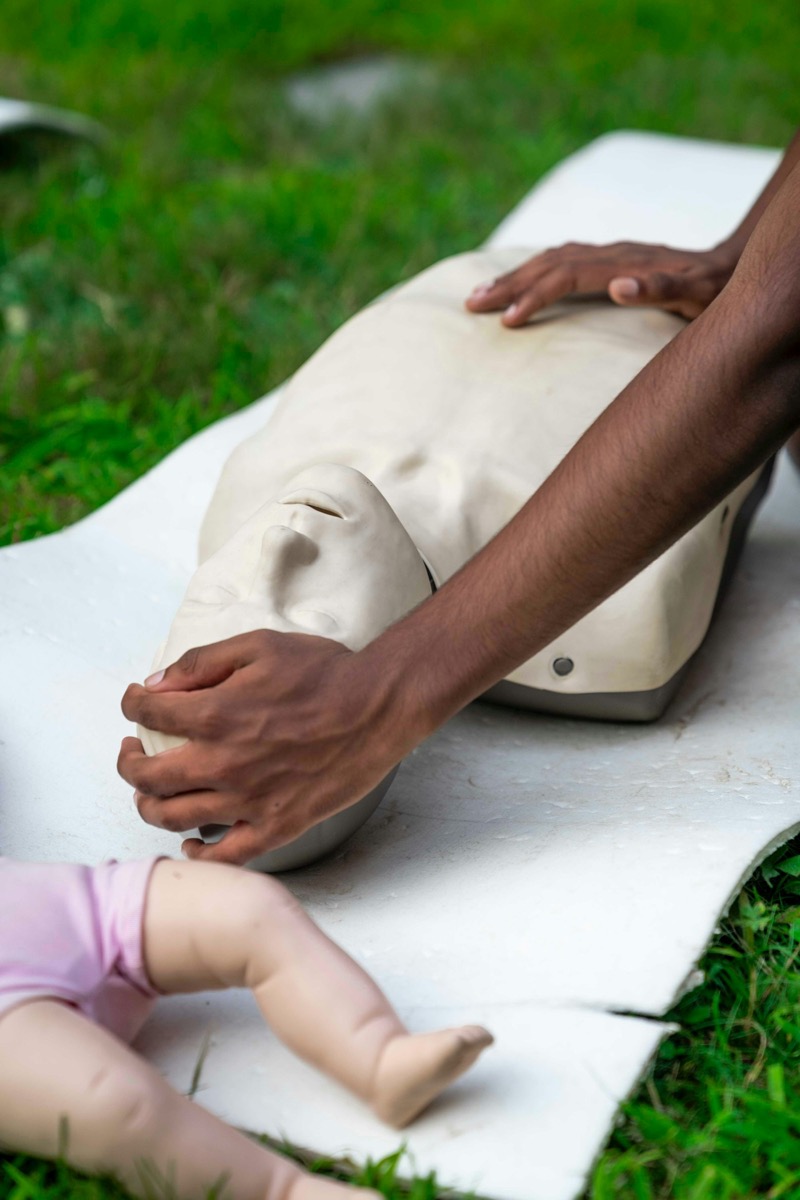 A trainee positioning an adult CPR manikin's airway, with an infant manikin beside it for paediatric practice.