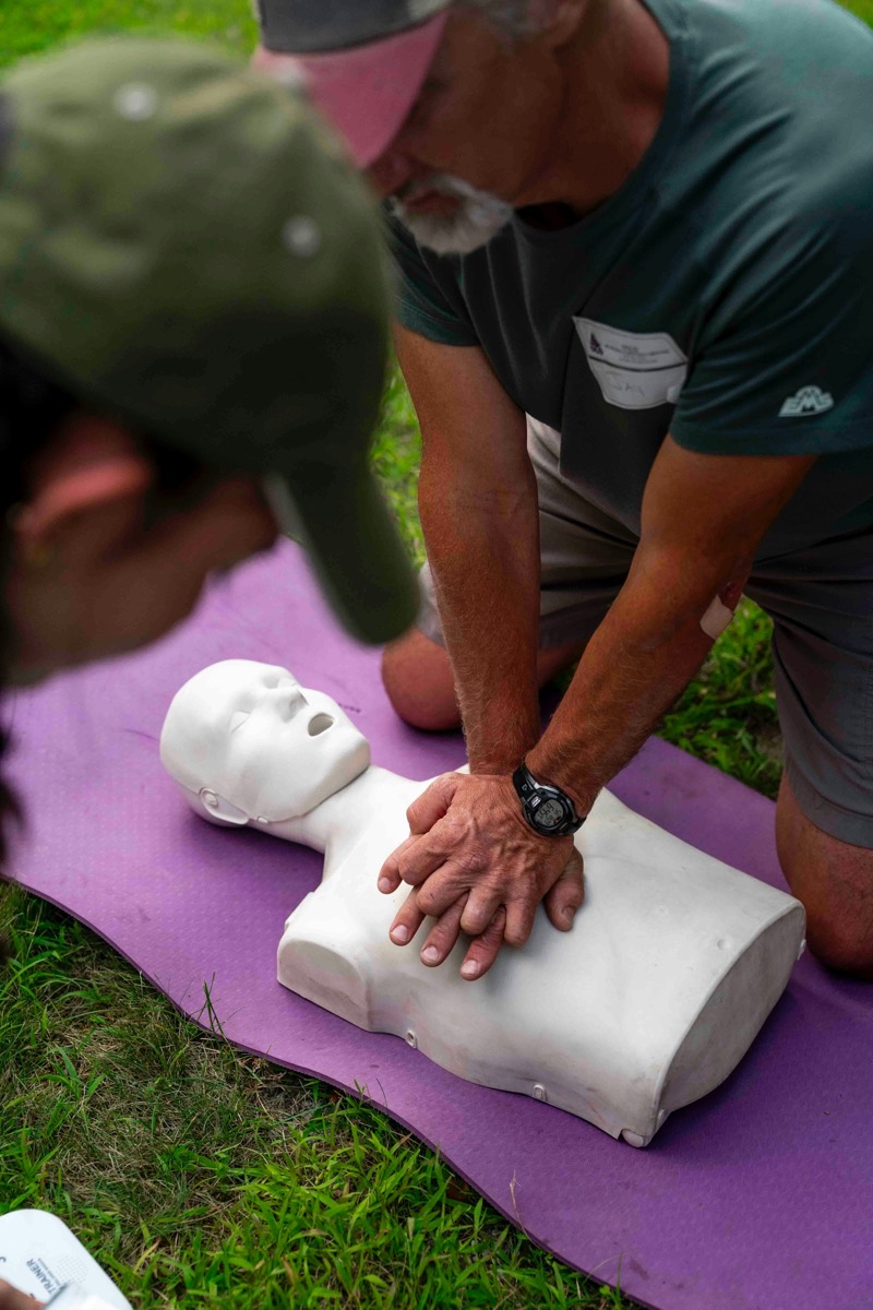 A trainer kneeling over a CPR manikin, demonstrating chest compressions to a student.