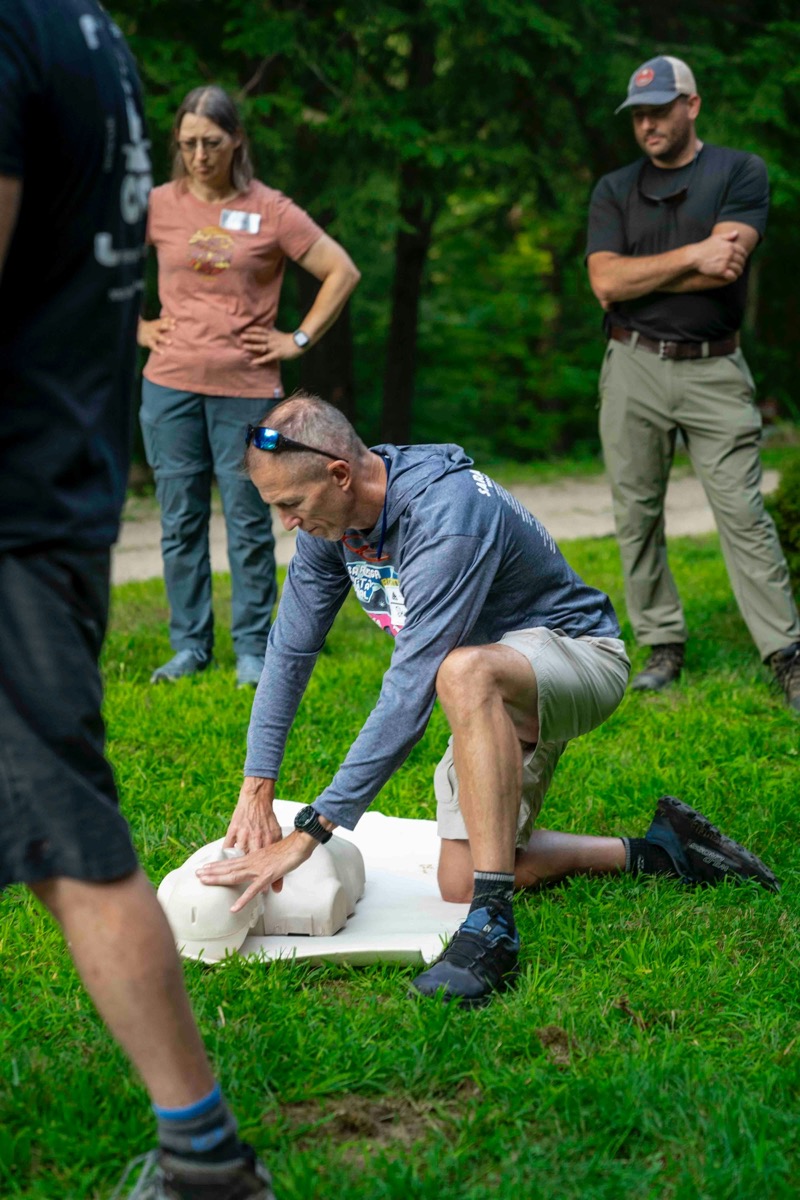A trainer demonstrating chest compressions on a manikin while a small group of students watches.